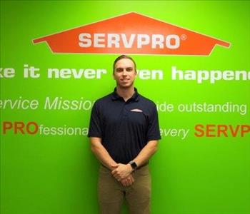 Male employee Mason Grossnickle standing in front of a green wall with the SERVPRO logo and mission statement below it.