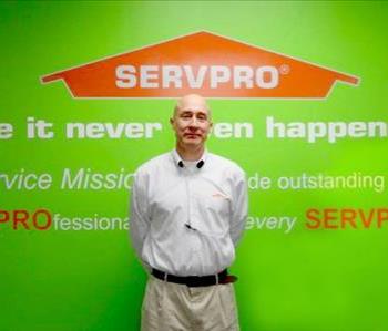 Male employee Mark Mitchell standing in front of a green wall with the SERVPRO logo and mission statement below it.