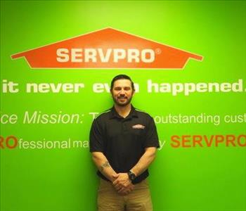 Male employee Aaron Tressler standing in front of a green wall with the SERVPRO logo and mission statement below it.