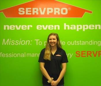 Female employee Brittany Paff standing in front of a green wall with the SERVPRO logo and mission statement below it.